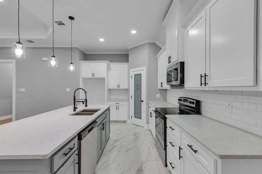 Kitchen with sink, an island with sink, decorative light fixtures, white cabinets, and appliances with stainless steel finishes