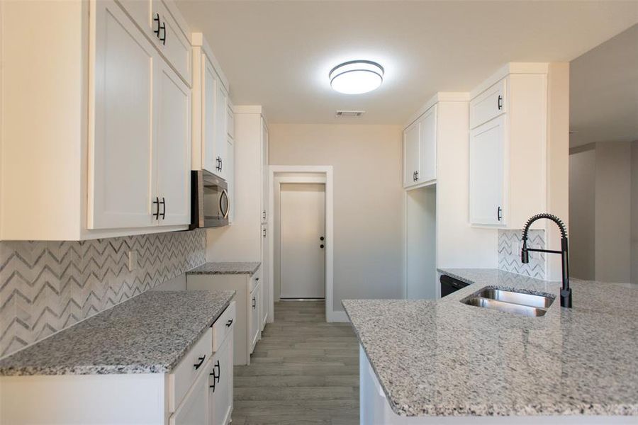 Kitchen featuring white cabinetry, sink, and light stone counters