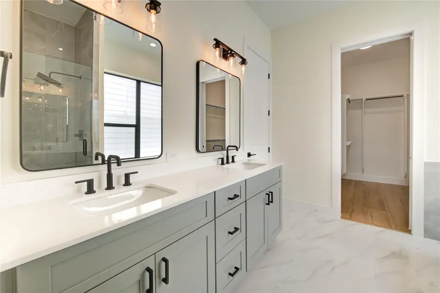 Sleek and modern primary bathroom featuring double sinks, elegant fixtures, and ample natural light. Sleek and modern primary bathroom featuring double sinks, elegant fixtures, and ample natural light.
