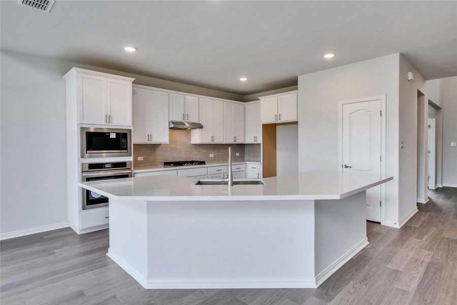 Kitchen featuring appliances with stainless steel finishes, a sink, under cabinet range hood, a spacious island, and light wood finished floors Kitchen featuring appliances with stainless steel finishes, a sink, under cabinet range hood, a spacious island, and light wood finished floors