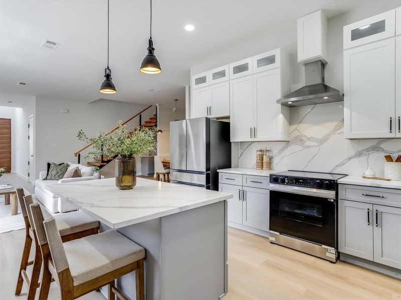 Modern kitchen featuring a waterfall island, light wood-finish flooring, stainless steel appliances, two-tone cabinetry, and a full-height tile backsplash Modern kitchen featuring a waterfall island, light wood-finish flooring, stainless steel appliances, two-tone cabinetry, and a full-height tile backsplash