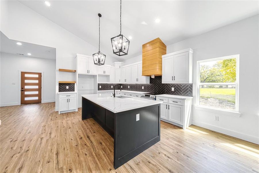 Kitchen featuring decorative backsplash, an island with sink, white cabinetry, pendant lighting, and light wood-style floors