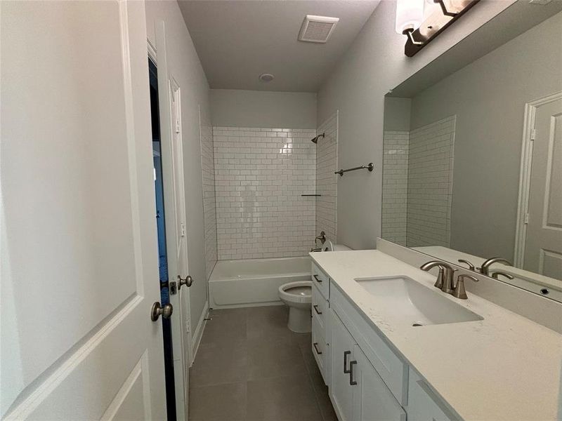 Full bathroom with vanity, tiled shower / bath combo, toilet, and tile patterned floors