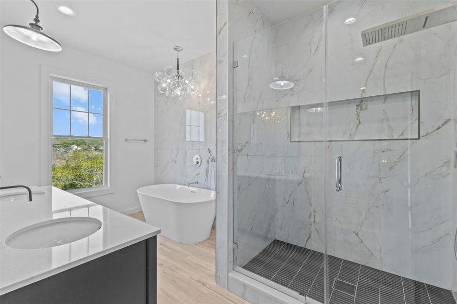 Bathroom with a marble finish shower, double vanity, a freestanding tub, light wood finished floors, and hanging lights