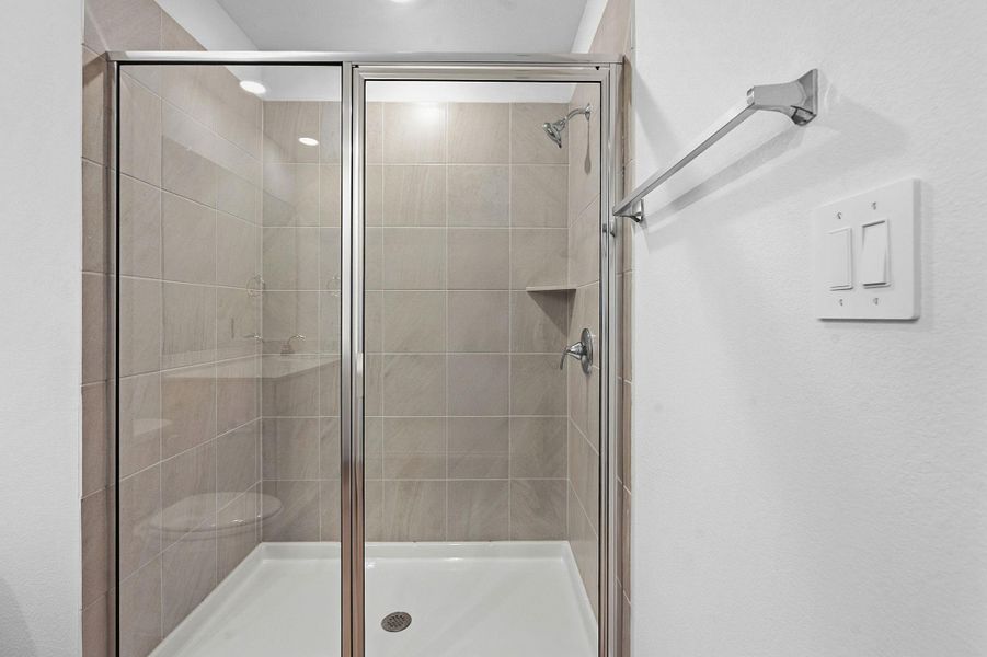 Glass-enclosed shower featuring large format tile surround, built-in shelving, chrome fixtures, and a white shower pan Glass-enclosed shower featuring large format tile surround, built-in shelving, chrome fixtures, and a white shower pan