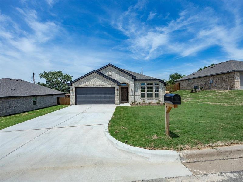 New construction residence featuring a light brick exterior, a two-car garage with a dark door, and a concrete driveway New construction residence featuring a light brick exterior, a two-car garage with a dark door, and a concrete driveway