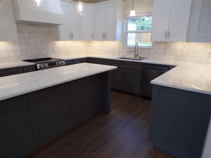 Kitchen featuring tasteful backsplash, ventilation hood, dark wood-type flooring, sink, and hanging light fixtures