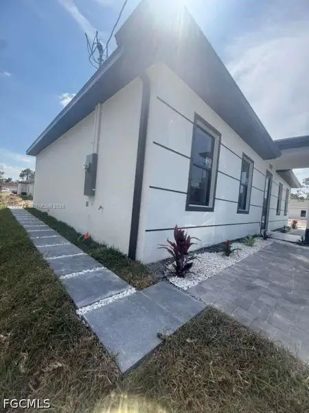Exterior featuring a smooth-stucco facade with horizontal architectural banding, dark-trimmed windows, a paved walkway, and decorative rock landscaping Exterior featuring a smooth-stucco facade with horizontal architectural banding, dark-trimmed windows, a paved walkway, and decorative rock landscaping