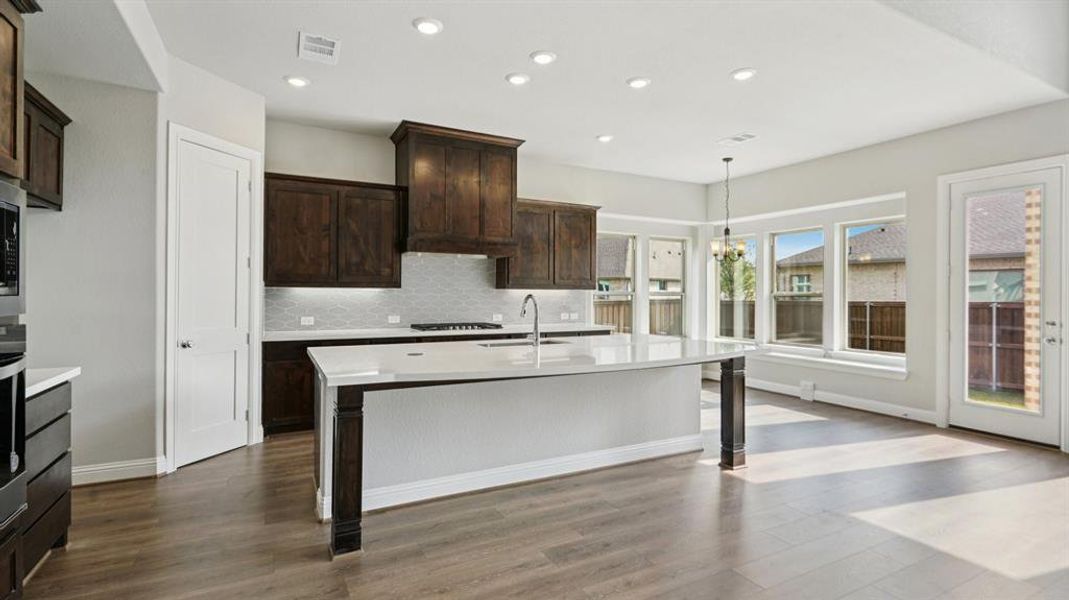 Kitchen with tasteful backsplash, decorative light fixtures, light stone counters, a chandelier, and dark wood-style flooring Kitchen with tasteful backsplash, decorative light fixtures, light stone counters, a chandelier, and dark wood-style flooring