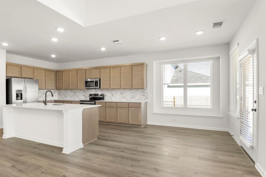 Kitchen featuring tasteful backsplash, stainless steel appliances, a kitchen island with sink, recessed lighting, and light wood finished floors