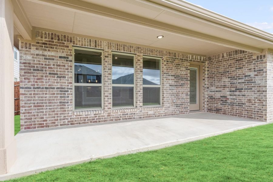 Covered back patio with concrete floor, brick exterior, large windows, and green lawn