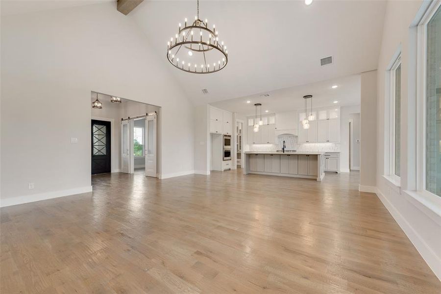 Unfurnished living room featuring high vaulted ceiling, beam ceiling, light hardwood / wood-style floors, and an inviting chandelier