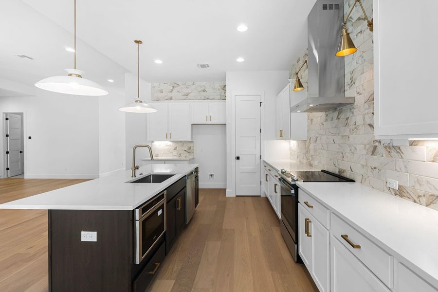 Kitchen with wall chimney exhaust hood, sink, white cabinetry, hanging light fixtures, and stainless steel appliances Kitchen with wall chimney exhaust hood, sink, white cabinetry, hanging light fixtures, and stainless steel appliances