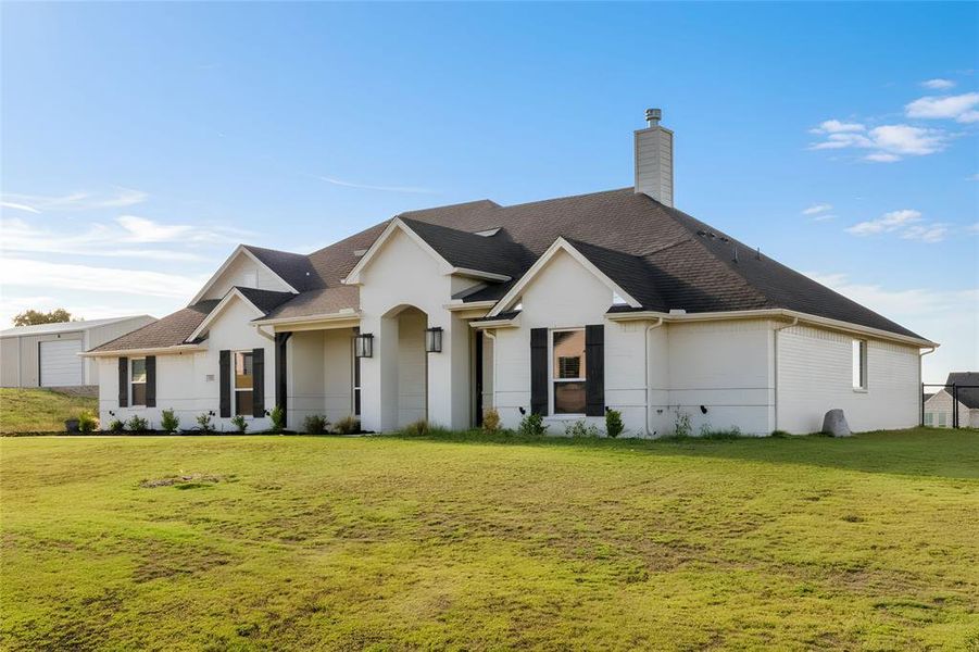 View of front of house with a front yard, roof with shingles, and a chimney