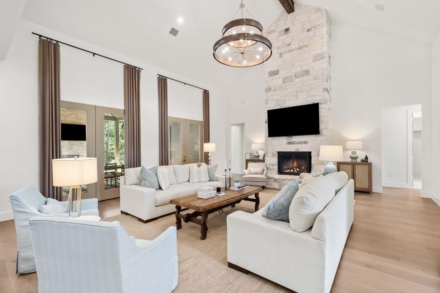 Impressive living room with soaring vaulted ceilings, exposed reclaimed barn wood wrapped beams and a dramatic floor-to-ceiling stone fireplace as the focal point. Oversized windows and French doors bring in natural light and connect seamlessly to the outdoor living area.