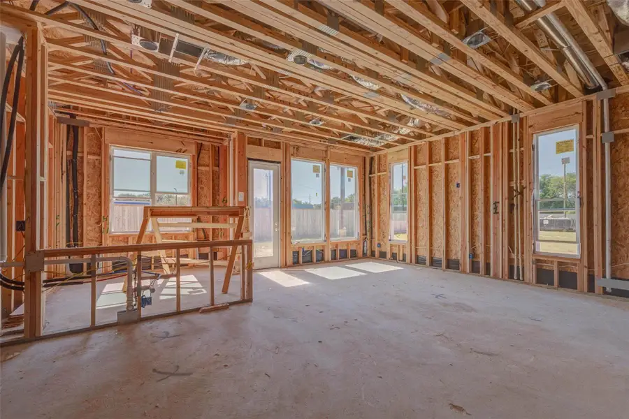 Bright open-concept living and kitchen area under construction with large windows, rear door, exposed framing, and visible mechanical systems overhead. This view captures the future heart of the home, where natural light, backyard access, and an efficient layout will come together to create a comfortable space for gathering, dining, and relaxing. Bright open-concept living and kitchen area under construction with large windows, rear door, exposed framing, and visible mechanical systems overhead. This view captures the future heart of the home, where natural light, backyard access, and an efficient layout will come together to create a comfortable space for gathering, dining, and relaxing.