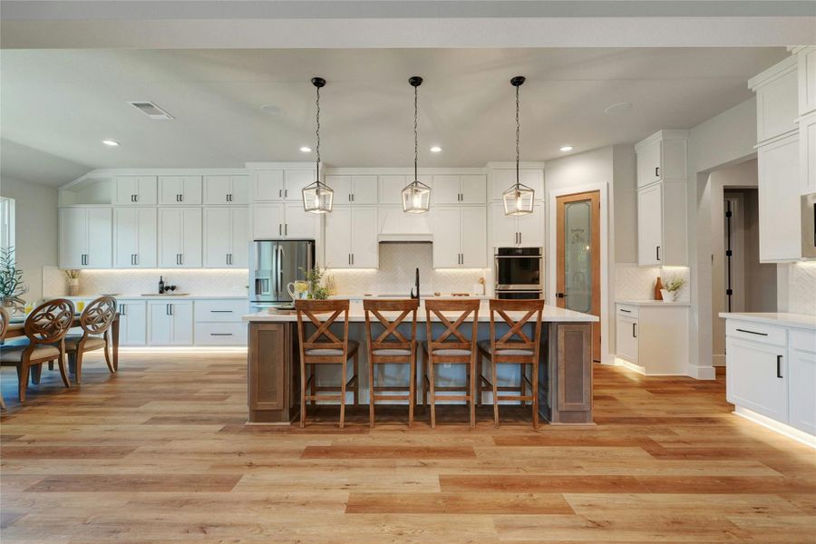 Gourmet kitchen featuring a large island with seating, pendant lighting, stainless steel appliances, extensive white cabinetry, and wood-finish flooring