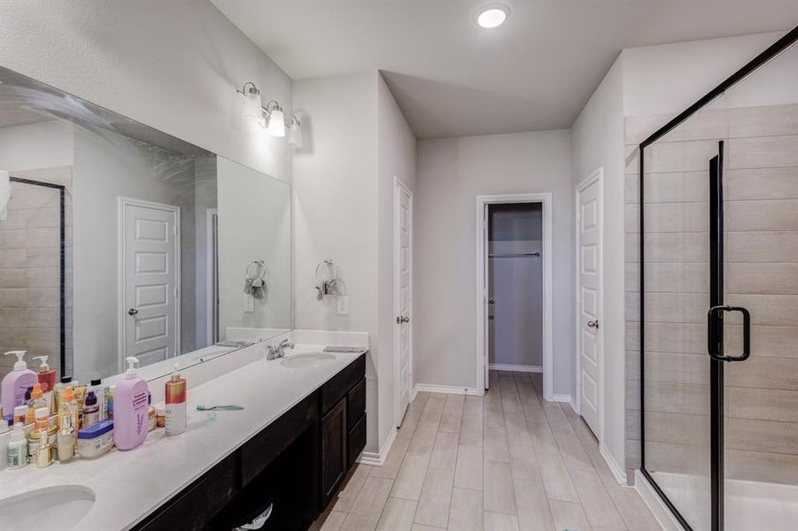 Bathroom featuring a stall shower, double vanity, a spacious closet, recessed lighting, and light wood-type flooring Bathroom featuring a stall shower, double vanity, a spacious closet, recessed lighting, and light wood-type flooring