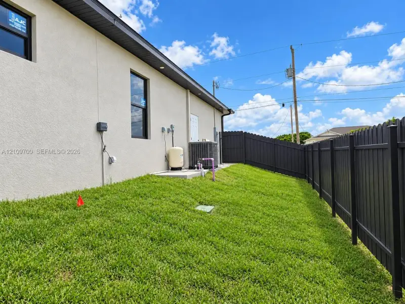Stucco exterior, black vinyl-framed windows, and a fenced side yard featuring an integrated utility area with a concrete equipment pad