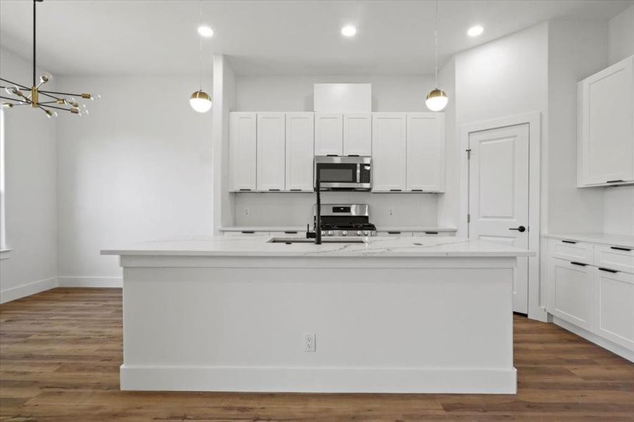 Kitchen with decorative light fixtures, white cabinetry, appliances with stainless steel finishes, light stone counters, and dark wood finished floors