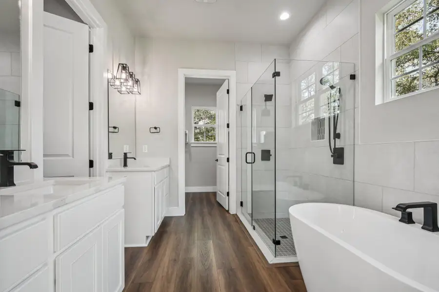 Bathroom featuring a shower stall, a freestanding tub, two vanities, dark wood-style floors, and tile walls