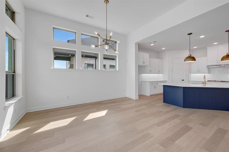 Two tone kitchen with suspended lighting, light wood finished floors, backsplash, light stone countertops, and two tone cabinetry