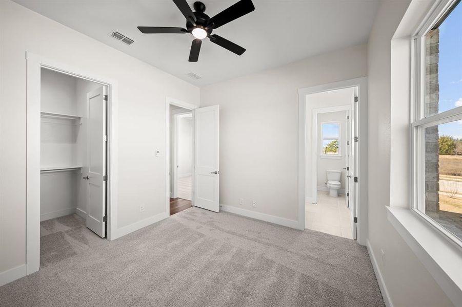 Unfurnished bedroom with light carpet, a walk in closet, a ceiling fan, and connected bathroom