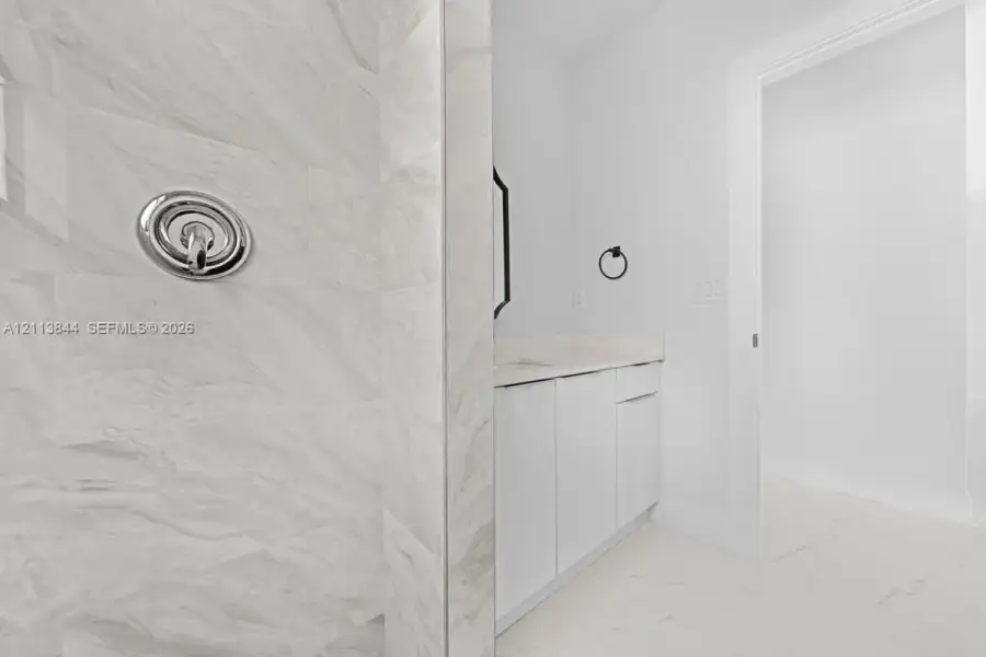 Shower featuring large-format stone-patterned wall tile and polished chrome plumbing fixtures, paired with a flat-panel vanity, light-toned countertop, and tile flooring Shower featuring large-format stone-patterned wall tile and polished chrome plumbing fixtures, paired with a flat-panel vanity, light-toned countertop, and tile flooring