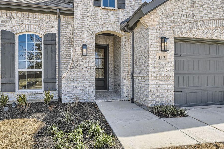 Doorway to property featuring brick siding, a garage, and roof with shingles