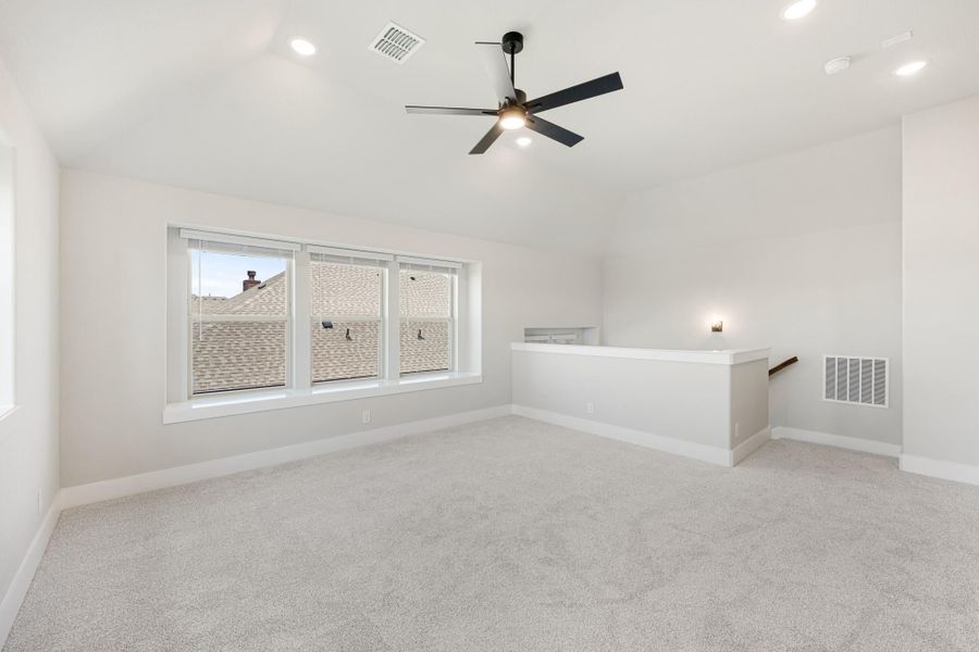 Open bonus room with carpet, ceiling fan, vaulted ceiling, and staircase landing overlook Open bonus room with carpet, ceiling fan, vaulted ceiling, and staircase landing overlook
