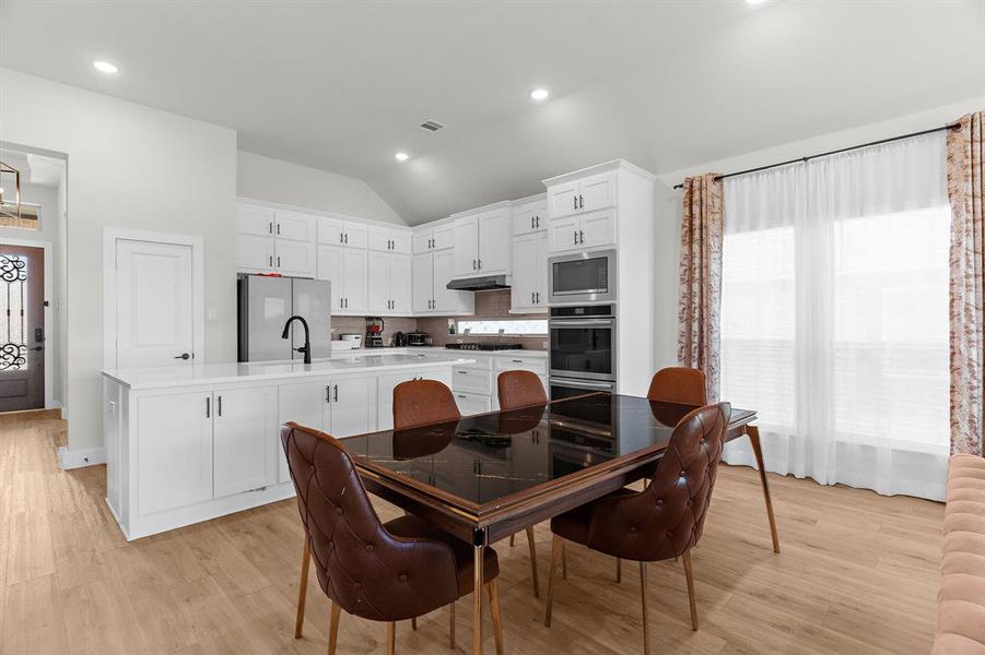 Dining space with lofted ceiling, light wood-style floors, and recessed lighting Dining space with lofted ceiling, light wood-style floors, and recessed lighting