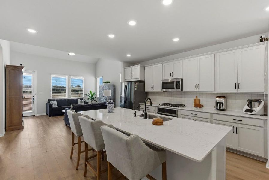 Kitchen featuring a kitchen breakfast bar, light stone countertops, open floor plan, light wood-style flooring, and recessed lighting