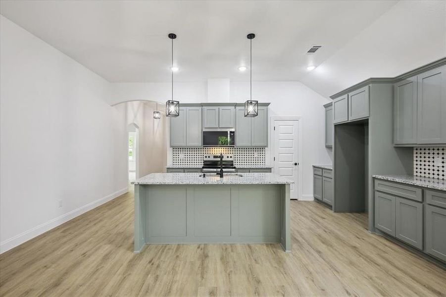 Kitchen with gray cabinetry, backsplash, arched walkways, light stone counters, and light wood-style flooring Kitchen with gray cabinetry, backsplash, arched walkways, light stone counters, and light wood-style flooring