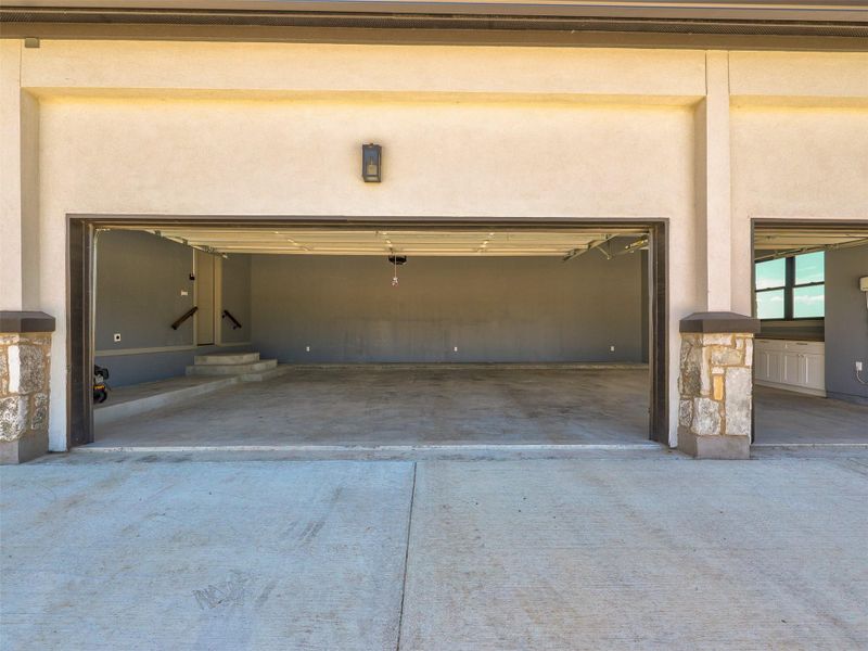 Concrete driveway leads to a multi-car garage with stone pillars and smooth stucco exterior walls.