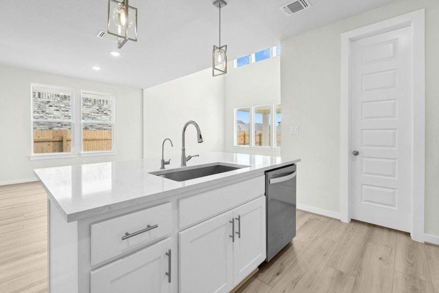 Kitchen with white cabinetry, light wood-type flooring, hanging light fixtures, light stone countertops, and an island with sink