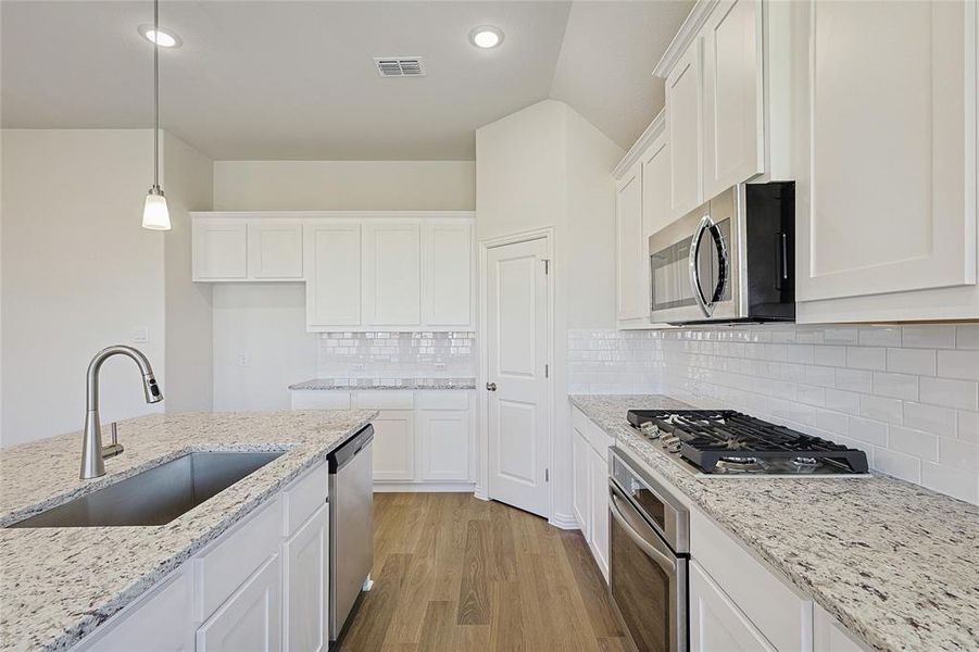 Kitchen with tasteful backsplash, appliances with stainless steel finishes, sink, white cabinetry, and decorative light fixtures