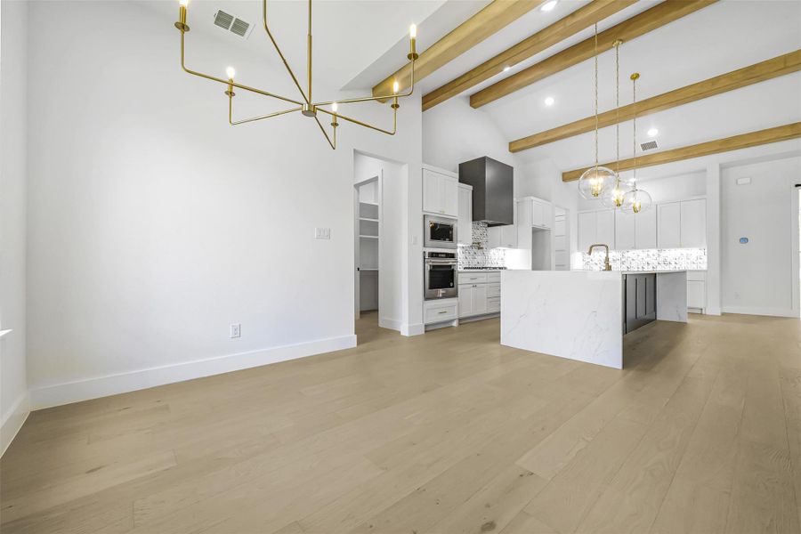 Kitchen featuring a chandelier, tasteful backsplash, white cabinetry, light wood-type flooring, and high vaulted ceiling