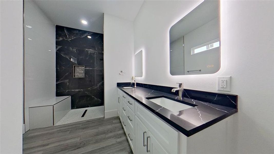 Contemporary bathroom featuring a dual vanity with dark stone countertops, undermount sinks, and illuminated mirrors Contemporary bathroom featuring a dual vanity with dark stone countertops, undermount sinks, and illuminated mirrors