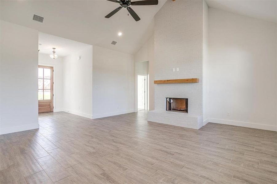 Unfurnished living room with a brick fireplace, high vaulted ceiling, light hardwood / wood-style floors, and ceiling fan