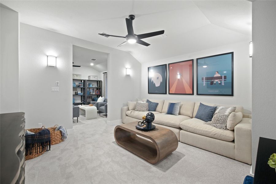 Carpeted media room with vaulted ceiling and ceiling fan