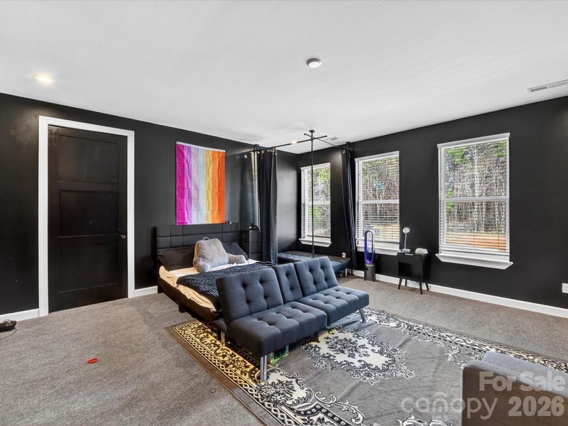Spacious modern bedroom with bold dark walls, large windows for natural light, and a cozy sitting area for added comfort.