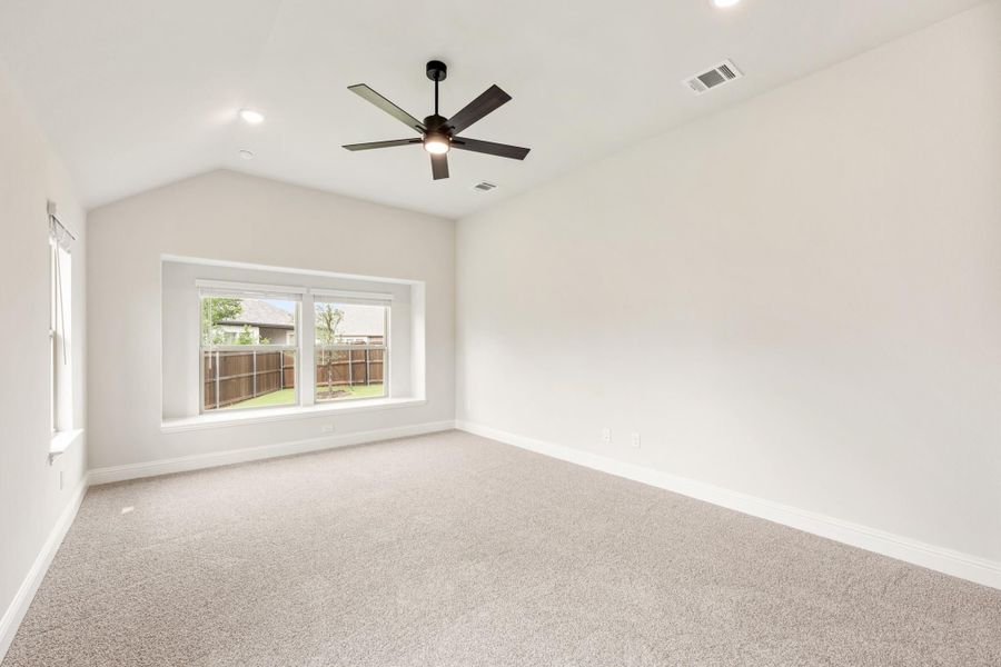 Empty bedroom with vaulted ceiling, ceiling fan, carpet flooring, and a window overlooking a backyard fence. Empty bedroom with vaulted ceiling, ceiling fan, carpet flooring, and a window overlooking a backyard fence.