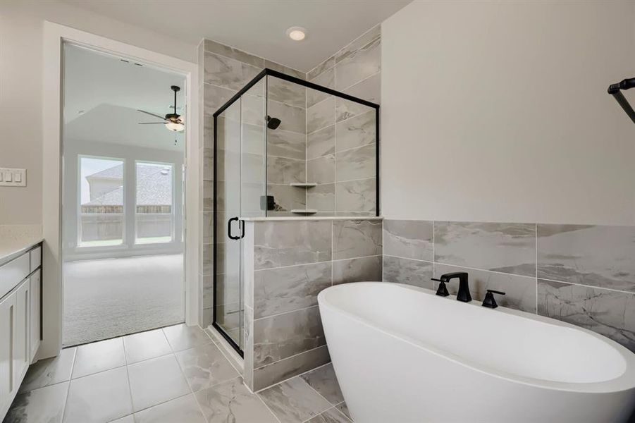 Contemporary bathroom featuring a freestanding soaking tub with matte black fixtures, a glass-enclosed shower with a black frame, and gray marble-look tile flooring and shower surround