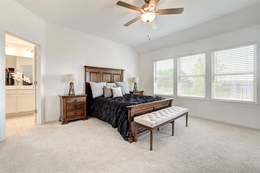 Bedroom featuring light colored carpet, lofted ceiling, ensuite bathroom, and a ceiling fan