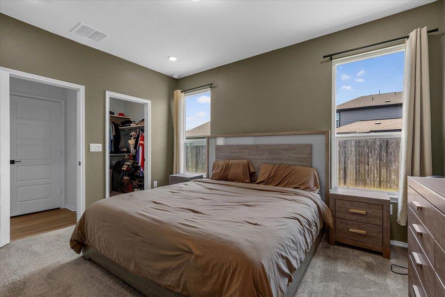 A well-lit bedroom features plush carpeting, a large window, and a convenient walk-in closet.