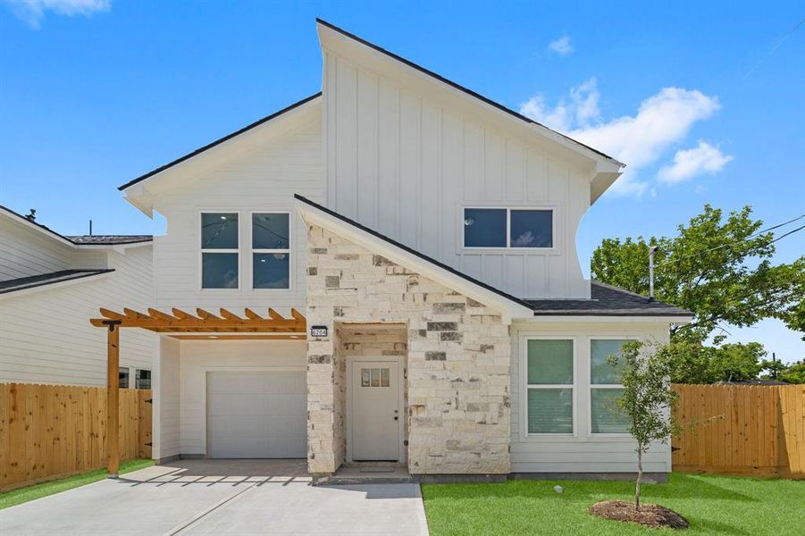 This is a modern two-story home with a fresh, white exterior, accented with natural stone. It features large windows for ample natural light, a single-car garage, and a neat, fenced yard.