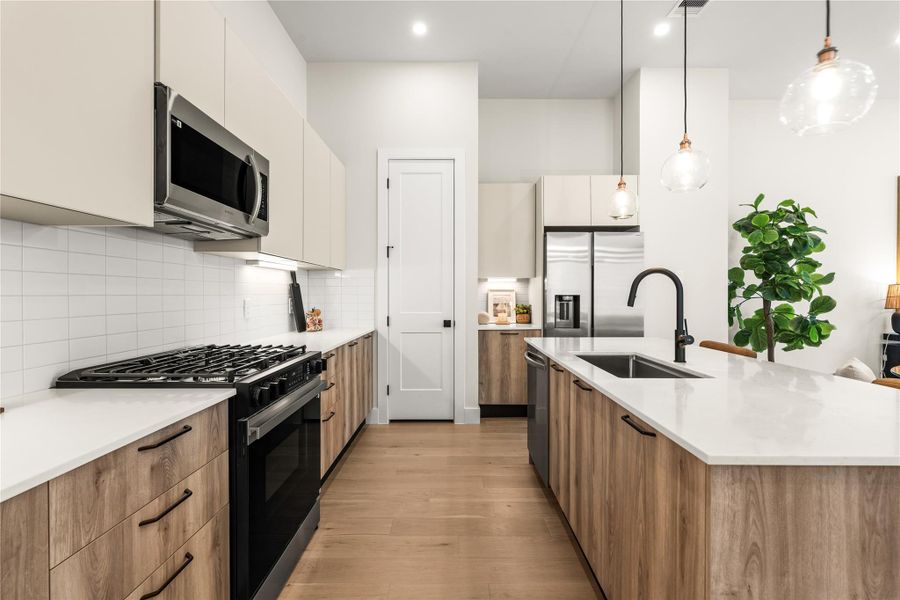 European flat-panel soft-close cabinetry combines warm wood tones with lighter uppers, while the long island creates a generous prep surface between the kitchen and living areas.