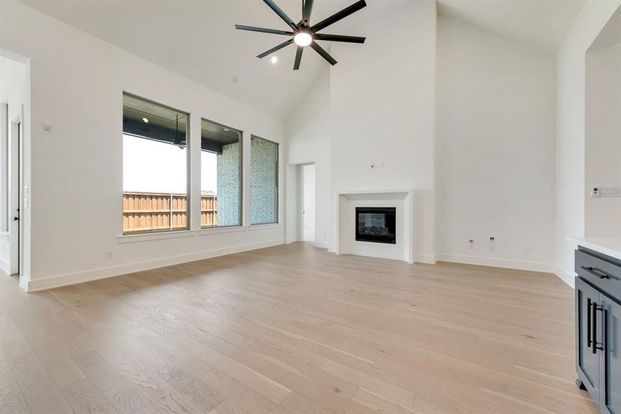 Unfurnished living room with high vaulted ceiling, light wood-style flooring, a glass covered fireplace, and ceiling fan Unfurnished living room with high vaulted ceiling, light wood-style flooring, a glass covered fireplace, and ceiling fan