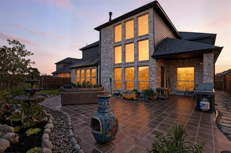 Back of house at dusk featuring roof with shingles, a patio, brick siding, and stone siding Back of house at dusk featuring roof with shingles, a patio, brick siding, and stone siding