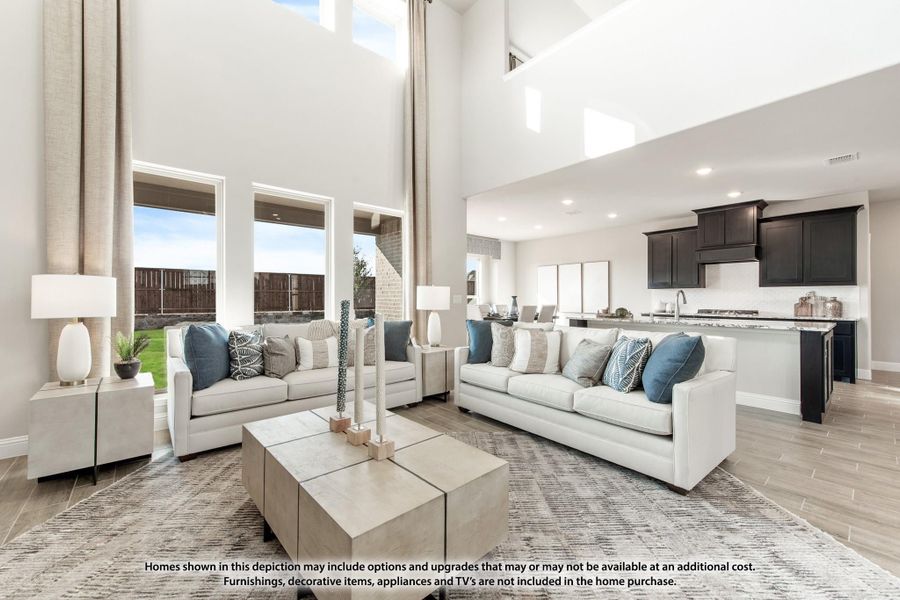 Open-concept living room with two-story ceiling, white sofas, and kitchen visible in background Open-concept living room with two-story ceiling, white sofas, and kitchen visible in background